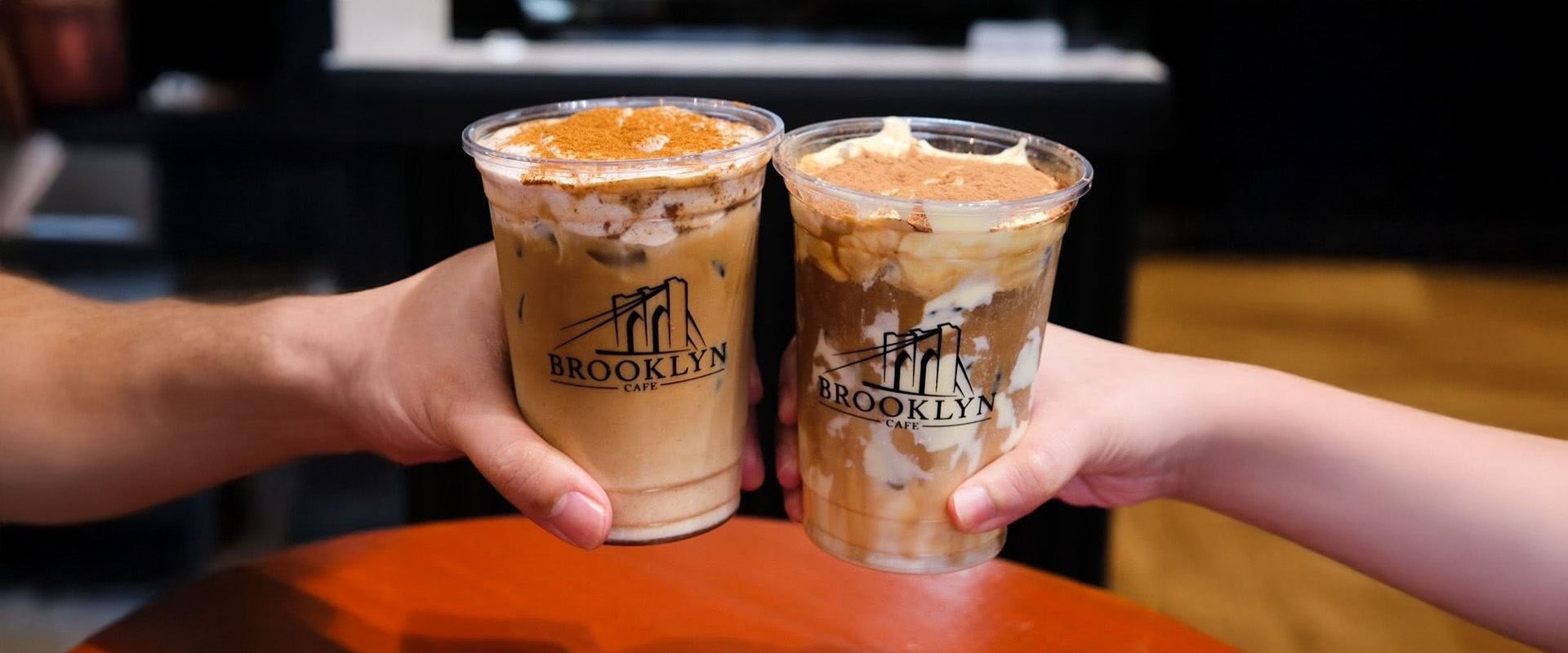 Two hands toasting iced Brooklyn Cafe coffees