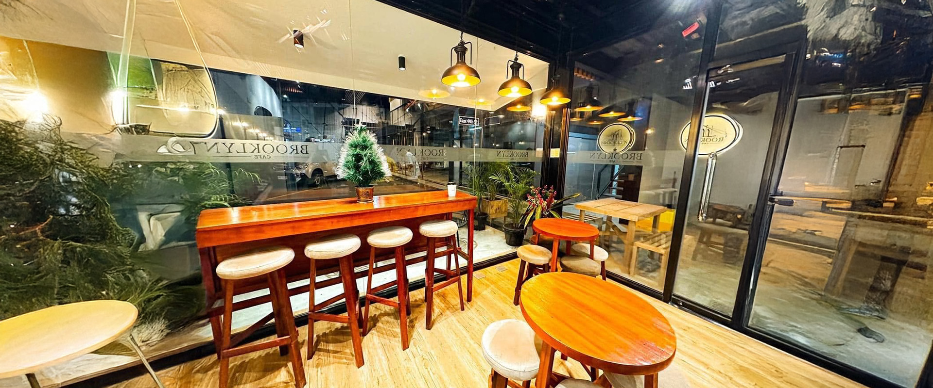 The window counter with high stools, wooden tables and pendant lights inside the cafe
