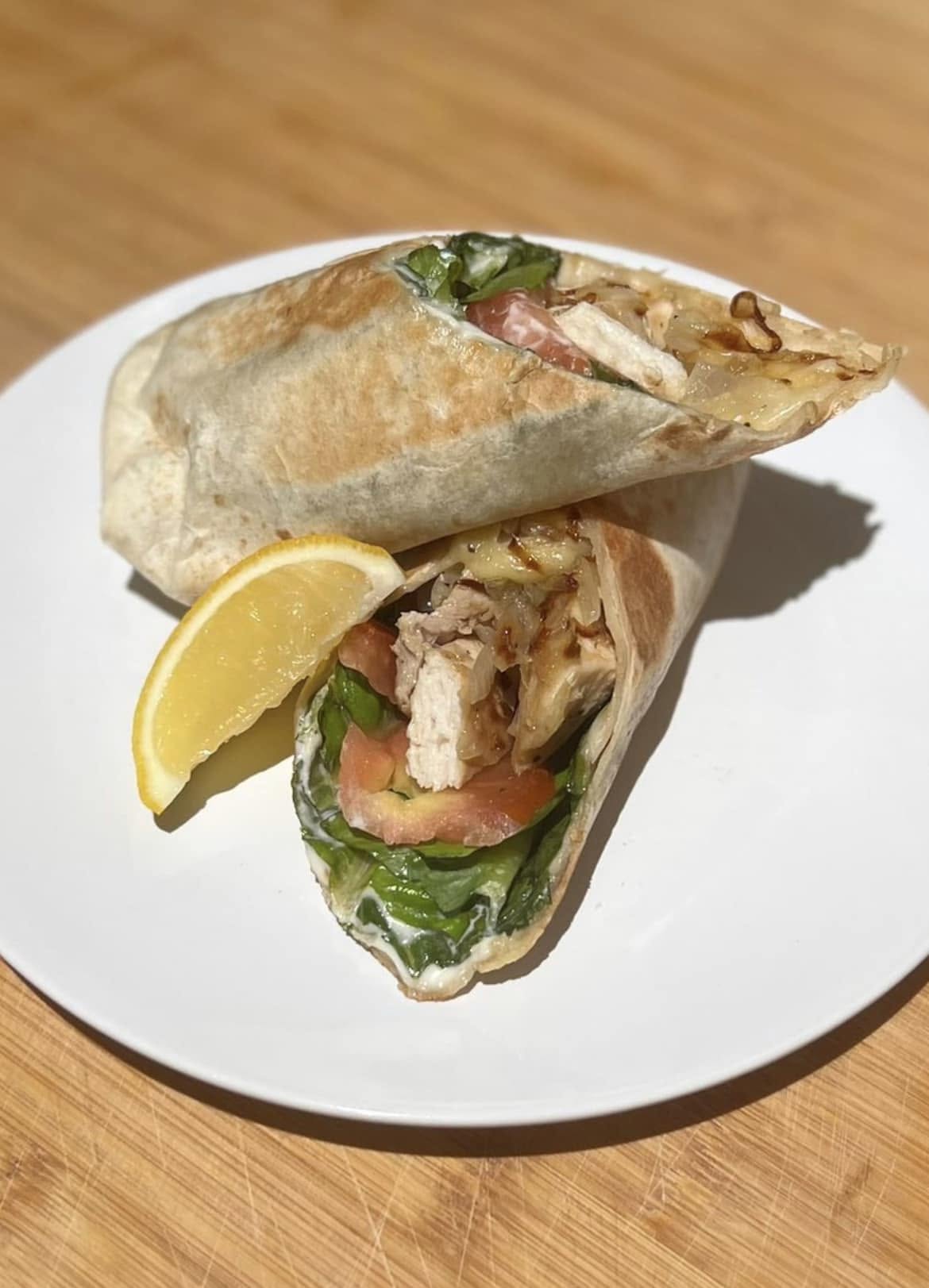A chicken wrap cut in half and served with a lemon wedge